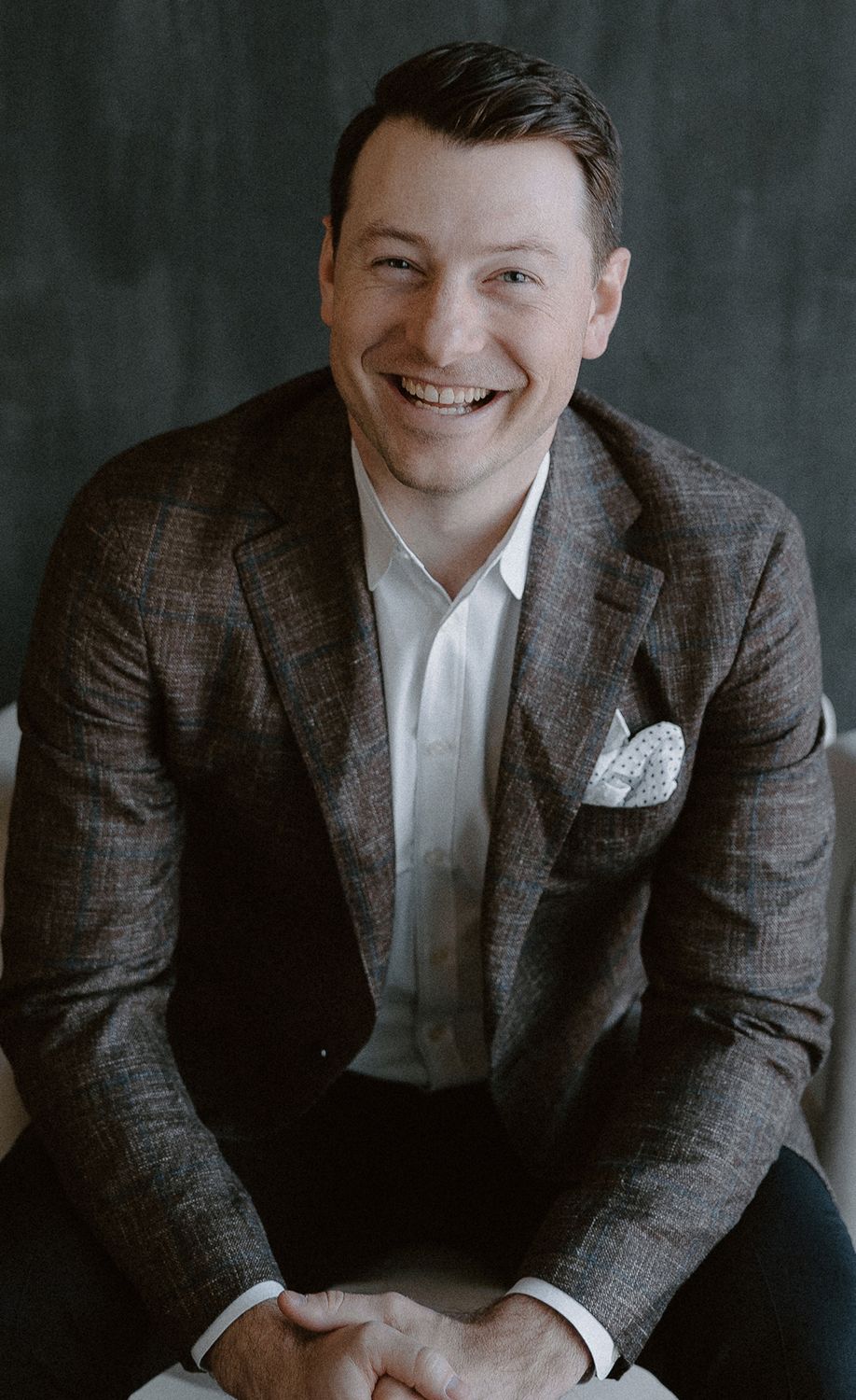 Smiling man in a brown jacket, seated.